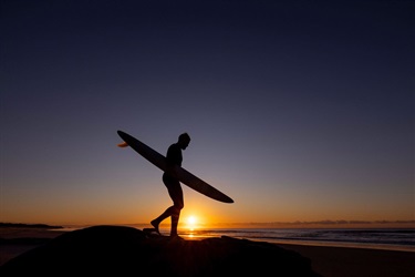 A solo surfer enters the water at Tuckers Rock at sunset.